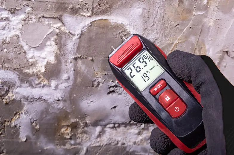 Feuchtemessgerät vor einer geschädigten Wand zur Bestimmung der Materialfeuchte und Untersuchung möglicher Feuchteschäden.