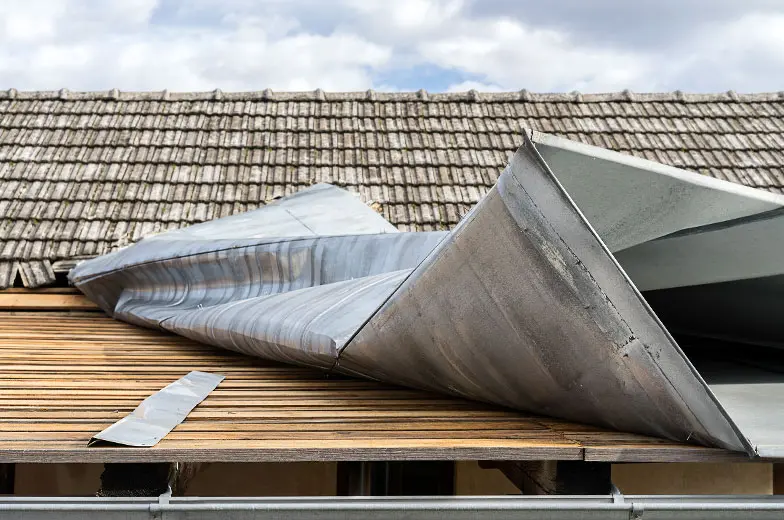 Sturmschaden an einem Gebäude mit stark verformten und abgelösten Blechelementen auf einer Dachfläche.
