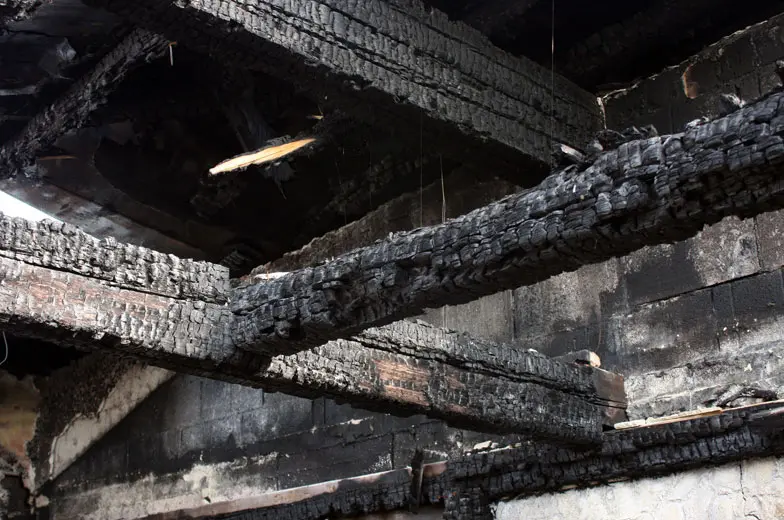 Massiver Brandschaden an einem Gebäude mit vollständig verkohlten Holzbalken und stark geschädigter Gebäudekonstruktion.