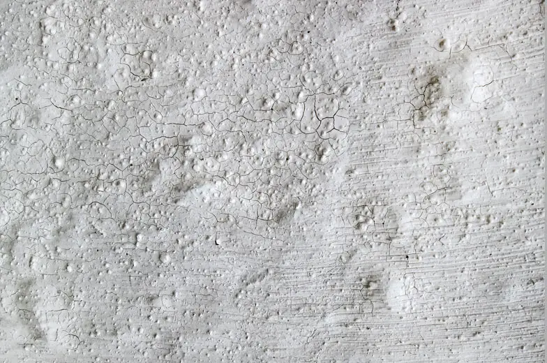 Raue, weiße Oberfläche mit unregelmäßigen Erhebungen und Rissen. Die Textur ähnelt einer körnigen, unebenen Wand oder einem kunstvollen Putz, geprägt von feinen Linien und kleinen Vertiefungen.