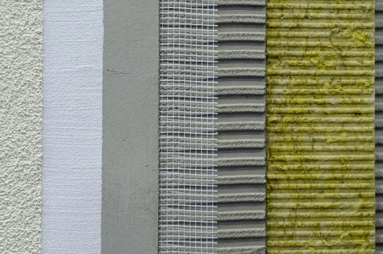 Nahaufnahme einer strukturierten Wand mit fünf vertikalen Abschnitten: weiß rau, beige glatt, graues Gitter, grauer Wellbelag und ein vernetzter, mit gelbem Material bedeckter Bereich.