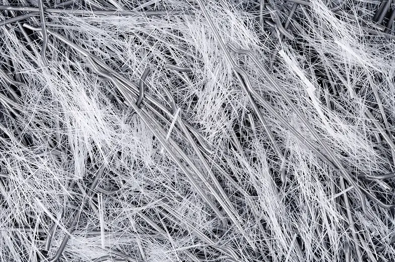 Ein komplexes Muster von ineinander verwobenen grauen und weißen, faserähnlichen Linien und Strängen, die ein dichtes und chaotisches Geflecht bilden. Das Bild erinnert an ein Wirrwarr aus Drähten oder Borsten.